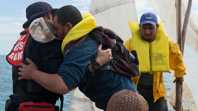 A member of the Coast Guar helps a migrant on a boat